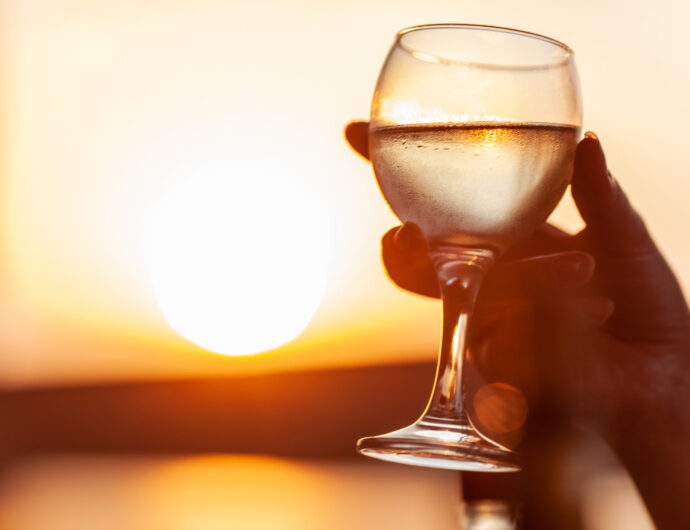 A misted glass of cold white wine in a womans hand, as gold as sunset in the background
