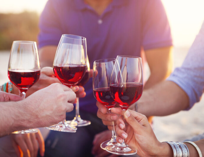 People holding glasses of red wine making a toast at the beach picnic