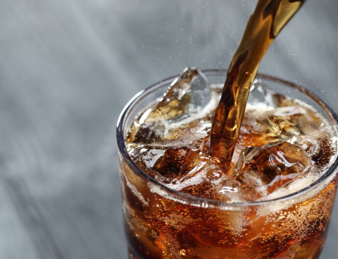 Pouring refreshing cola into glass on blurred grey background, closeup. Space for text